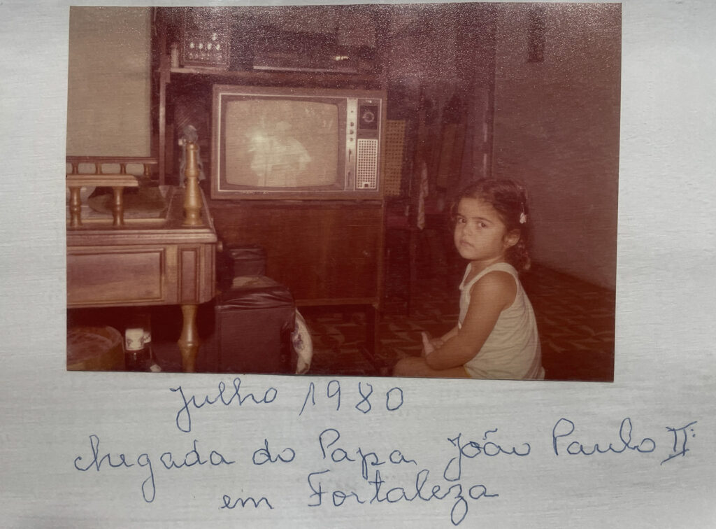 Fotografia impressa que mostra a filha de Maria da Penha sentada em sua casa